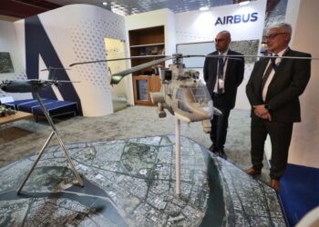 Representatives from French arms and military manufacturers stand near models of weapons at their stand during the 10th edition of the Baghdad security, defence and military industry fair organised on the premises of the Baghdad international exhibition complex in the Iraqi capital on March 2, 2022. (Photo by AHMAD AL-RUBAYE / AFP)